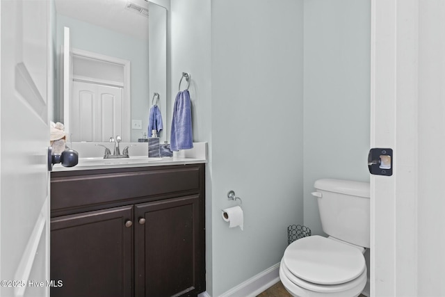 half bath with baseboards, visible vents, toilet, and vanity