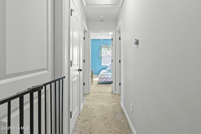 corridor featuring baseboards, attic access, and light colored carpet