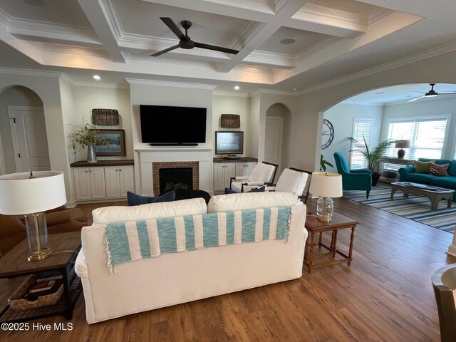 1325 Grandiflora Dr, Leland, NC 28451 - living area featuring coffered ceiling, arched walkways, a ceiling fan, a fireplace, and wood finished floors