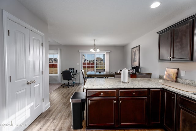 kitchen featuring light wood-style flooring, a chandelier, a peninsula, baseboards, and pendant lighting