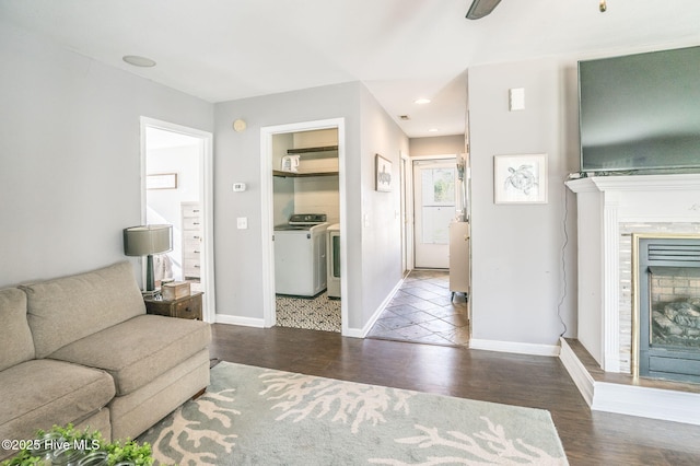 living area with baseboards, a fireplace with raised hearth, wood finished floors, recessed lighting, and washer and dryer