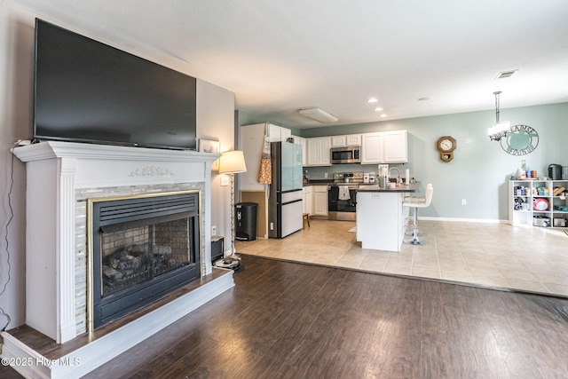 living area featuring baseboards, visible vents, light wood-style flooring, and a premium fireplace