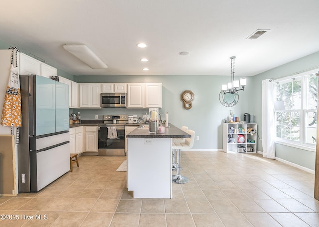 kitchen with light tile patterned flooring, a kitchen breakfast bar, appliances with stainless steel finishes, dark countertops, and visible vents
