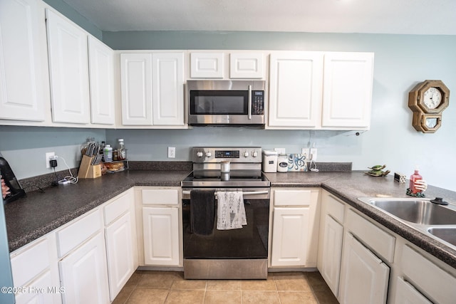 kitchen with white cabinets, dark countertops, appliances with stainless steel finishes, a sink, and light tile patterned floors