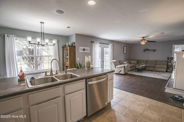 kitchen with light tile patterned flooring, a sink, stainless steel dishwasher, ceiling fan with notable chandelier, and dark countertops