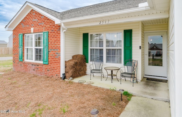 entrance to property with brick siding, a porch, and roof with shingles