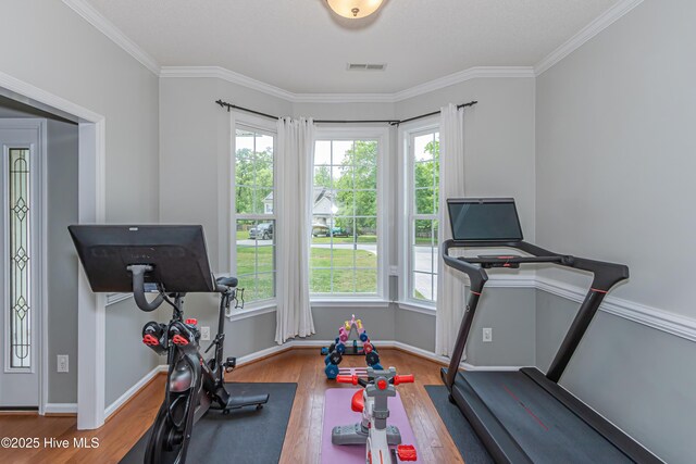 exercise room featuring baseboards, visible vents, ornamental molding, and wood finished floors
