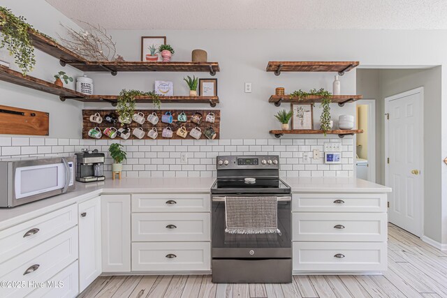 kitchen with open shelves, white microwave, stainless steel electric stove, and light countertops