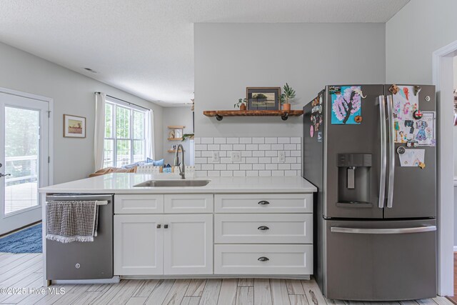 kitchen with backsplash, appliances with stainless steel finishes, a sink, light countertops, and white cabinetry