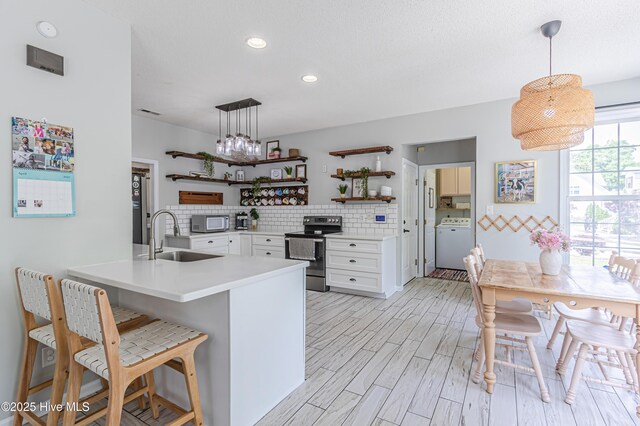 kitchen with appliances with stainless steel finishes, open shelves, a sink, a peninsula, and washer / dryer