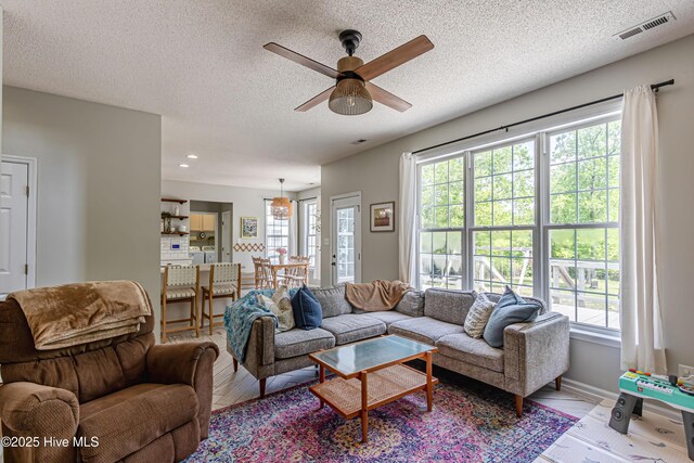 living room with visible vents, a ceiling fan, a textured ceiling, and light wood-style floors
