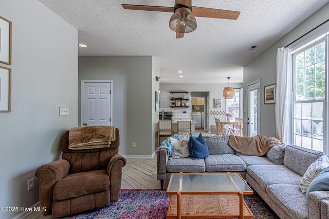 living room with visible vents, baseboards, ceiling fan, and a healthy amount of sunlight