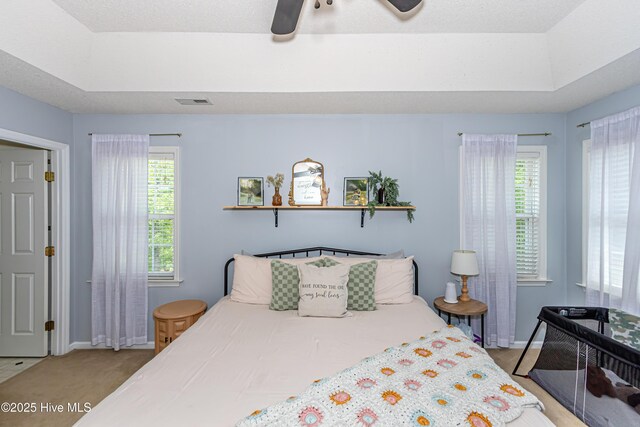 bedroom featuring light colored carpet, a raised ceiling, a ceiling fan, baseboards, and visible vents