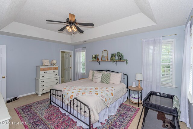 bedroom with baseboards, a textured ceiling, a tray ceiling, and light carpet