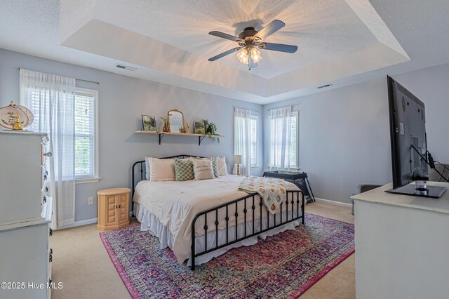 bedroom with a tray ceiling, visible vents, light carpet, and baseboards