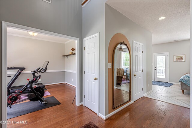 workout room with wood finished floors, baseboards, recessed lighting, a textured ceiling, and arched walkways