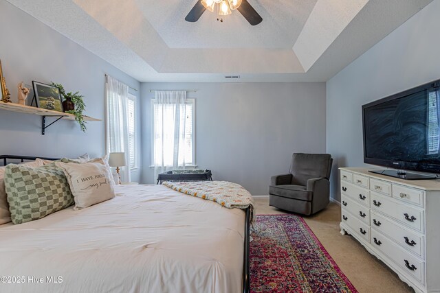 bedroom featuring a ceiling fan, a tray ceiling, and light carpet