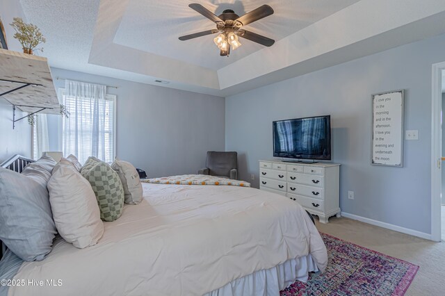 carpeted bedroom featuring baseboards, ceiling fan, a tray ceiling, and visible vents