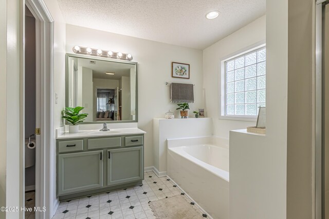full bath featuring a textured ceiling, baseboards, a garden tub, and vanity