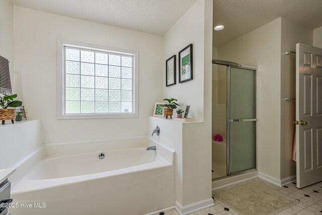 bathroom featuring a textured ceiling, a shower stall, baseboards, and a garden tub
