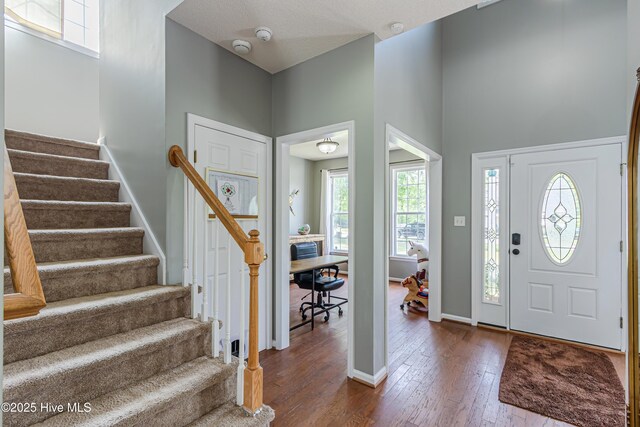 foyer featuring baseboards, a high ceiling, dark wood-style floors, and stairs