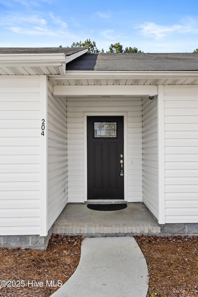 view of exterior entry featuring a shingled roof