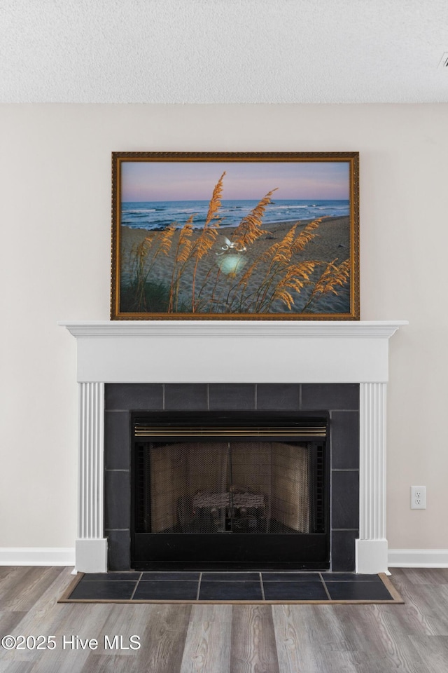 interior details featuring baseboards, a textured ceiling, wood finished floors, and a tiled fireplace