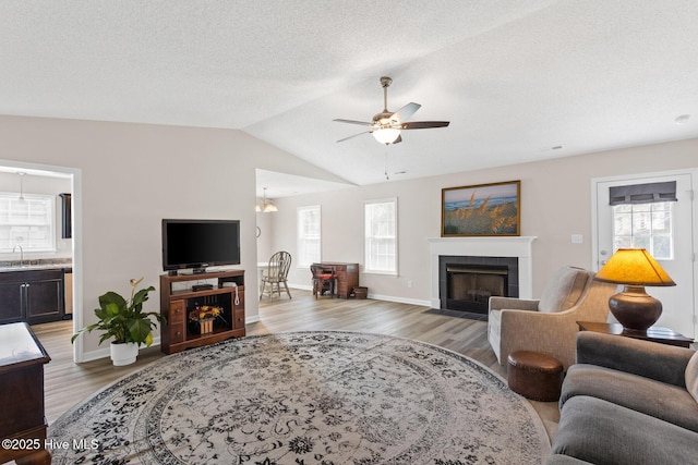 living room with a tiled fireplace, light wood-type flooring, a healthy amount of sunlight, and ceiling fan