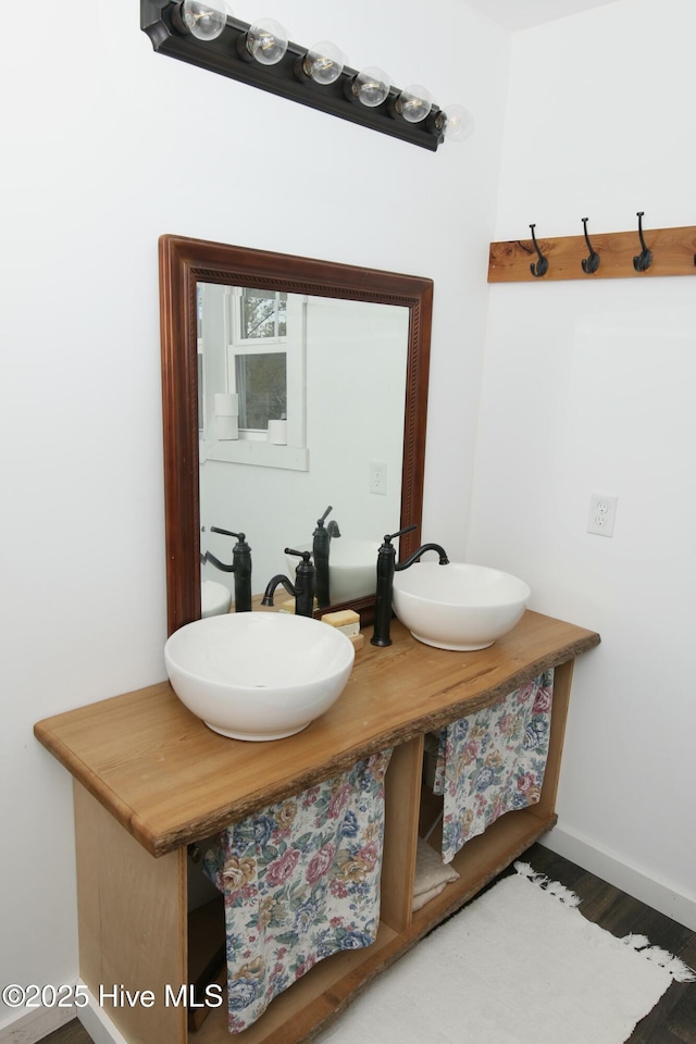 bathroom featuring baseboards, double vanity, a sink, and wood finished floors