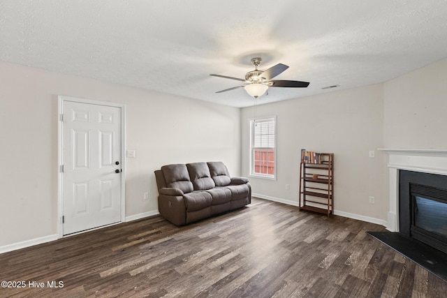 sitting room with dark wood-type flooring, a glass covered fireplace, a textured ceiling, and a ceiling fan
