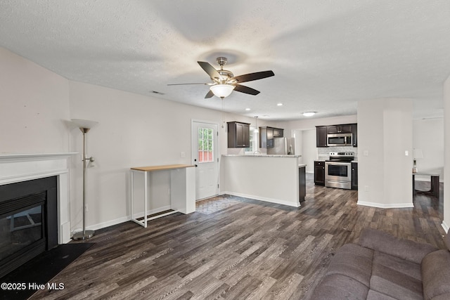 unfurnished living room featuring a textured ceiling, dark wood-style flooring, a glass covered fireplace, baseboards, and a ceiling fan
