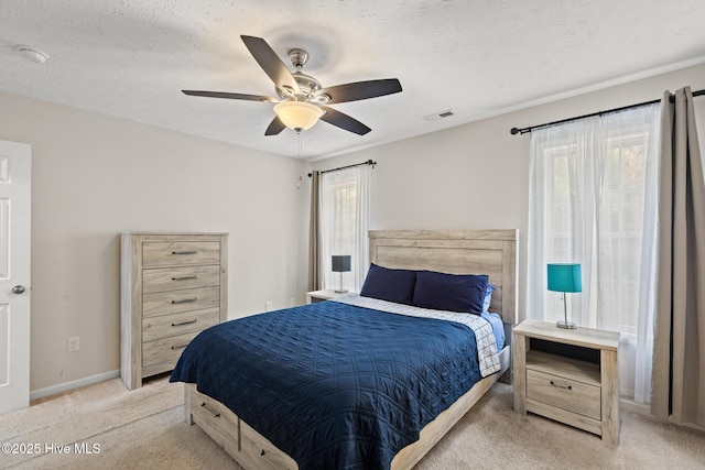 bedroom featuring visible vents, baseboards, a textured ceiling, light colored carpet, and ceiling fan