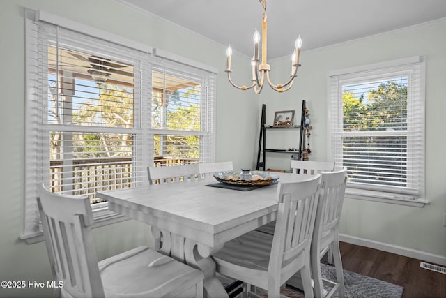 dining room featuring a healthy amount of sunlight, wood finished floors, ornamental molding, and an inviting chandelier
