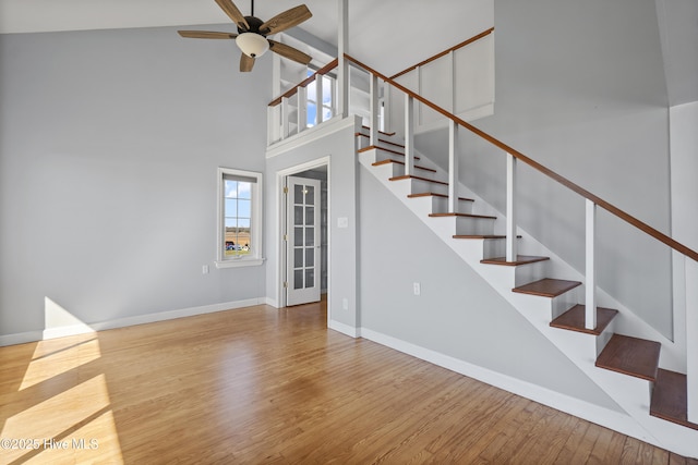 staircase featuring a towering ceiling, baseboards, ceiling fan, and wood finished floors