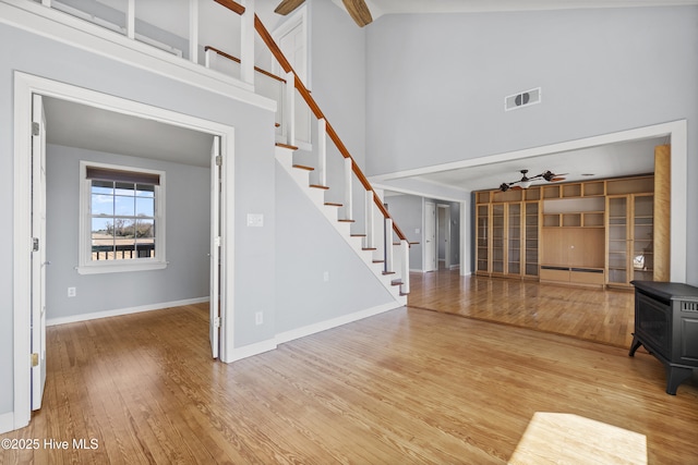 unfurnished living room featuring a high ceiling, wood finished floors, stairs, and ceiling fan