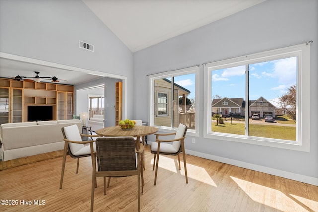 dining room featuring light wood finished floors, baseboards, visible vents, and high vaulted ceiling