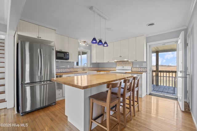 kitchen featuring stove, under cabinet range hood, wood counters, freestanding refrigerator, and black microwave