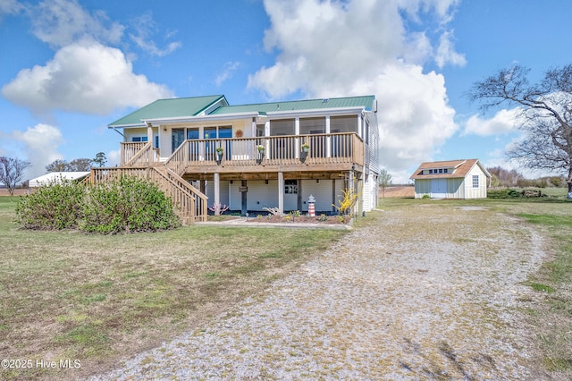 back of property with an outbuilding, metal roof, driveway, a deck, and a lawn