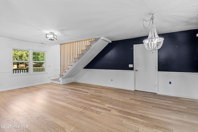 unfurnished living room featuring stairway, a chandelier, and wood finished floors