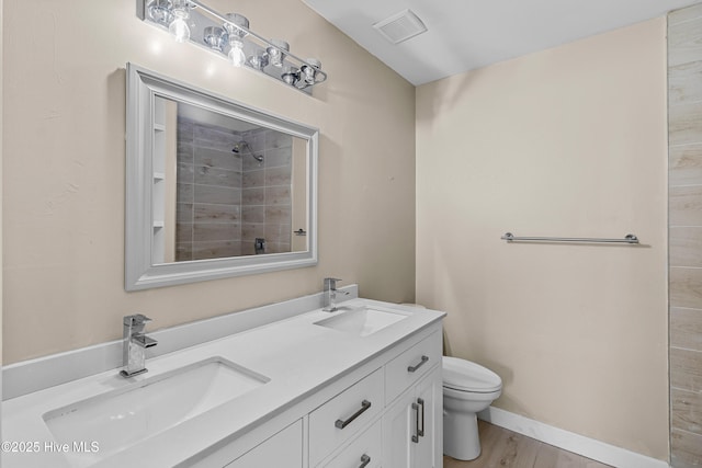 bathroom featuring toilet, a tile shower, visible vents, and a sink