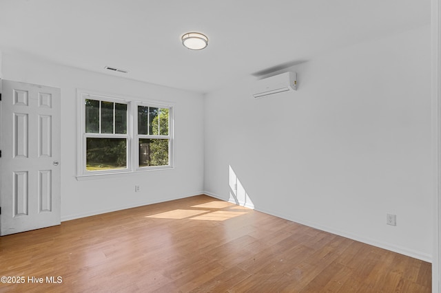 unfurnished room with baseboards, visible vents, a wall mounted AC, and wood finished floors