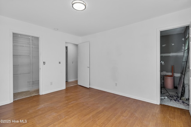 unfurnished bedroom with a closet, baseboards, connected bathroom, a spacious closet, and light wood-type flooring