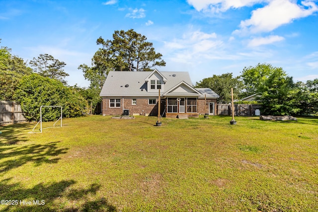 back of property with a lawn, a sunroom, brick siding, and fence