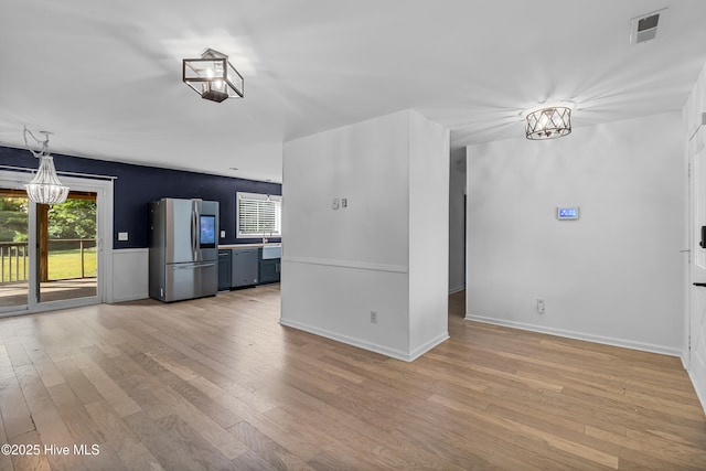 unfurnished living room with baseboards, a notable chandelier, light wood-style floors, and visible vents