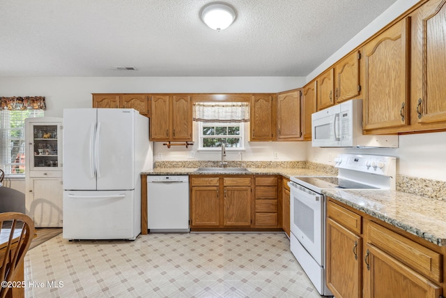 kitchen featuring a sink, white appliances, a textured ceiling, brown cabinetry, and visible vents