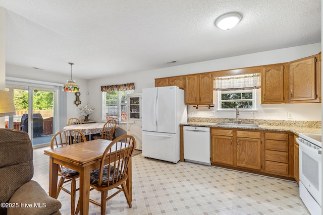 kitchen featuring a sink, white appliances, a textured ceiling, brown cabinetry, and light floors