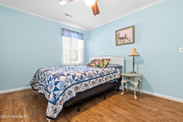 bedroom with baseboards, ornamental molding, visible vents, and wood finished floors