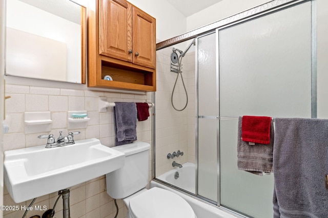 full bath featuring combined bath / shower with glass door, toilet, a sink, decorative backsplash, and tile walls