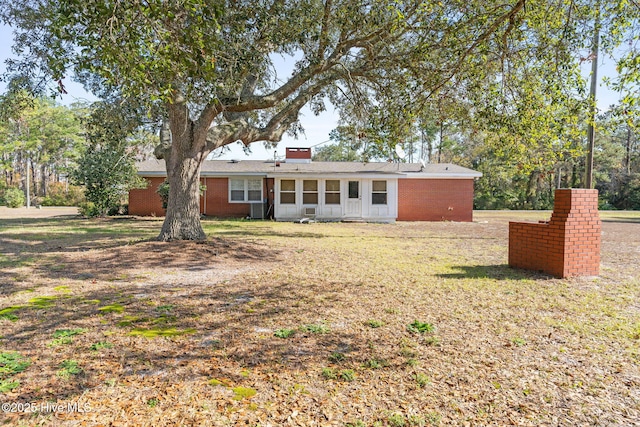 rear view of house featuring a chimney, brick siding, and a yard