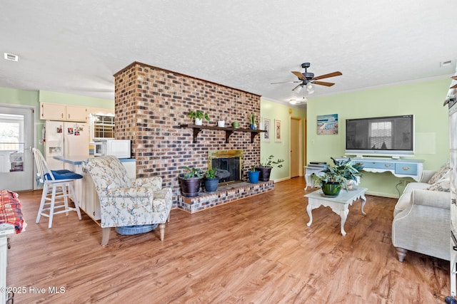 living room with a fireplace, a textured ceiling, a ceiling fan, and light wood finished floors